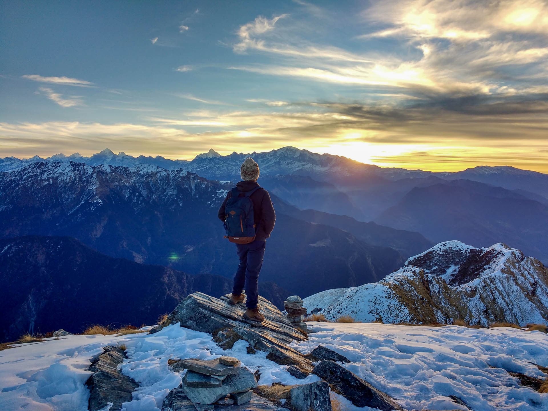 The sun rising over the horizon while a person looks at it over the mountain peak