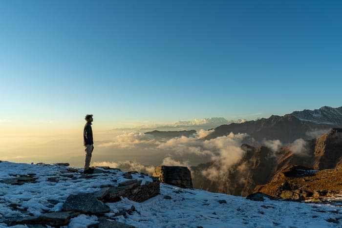 One person standing on the edge of a mountain as the sun sets behind them